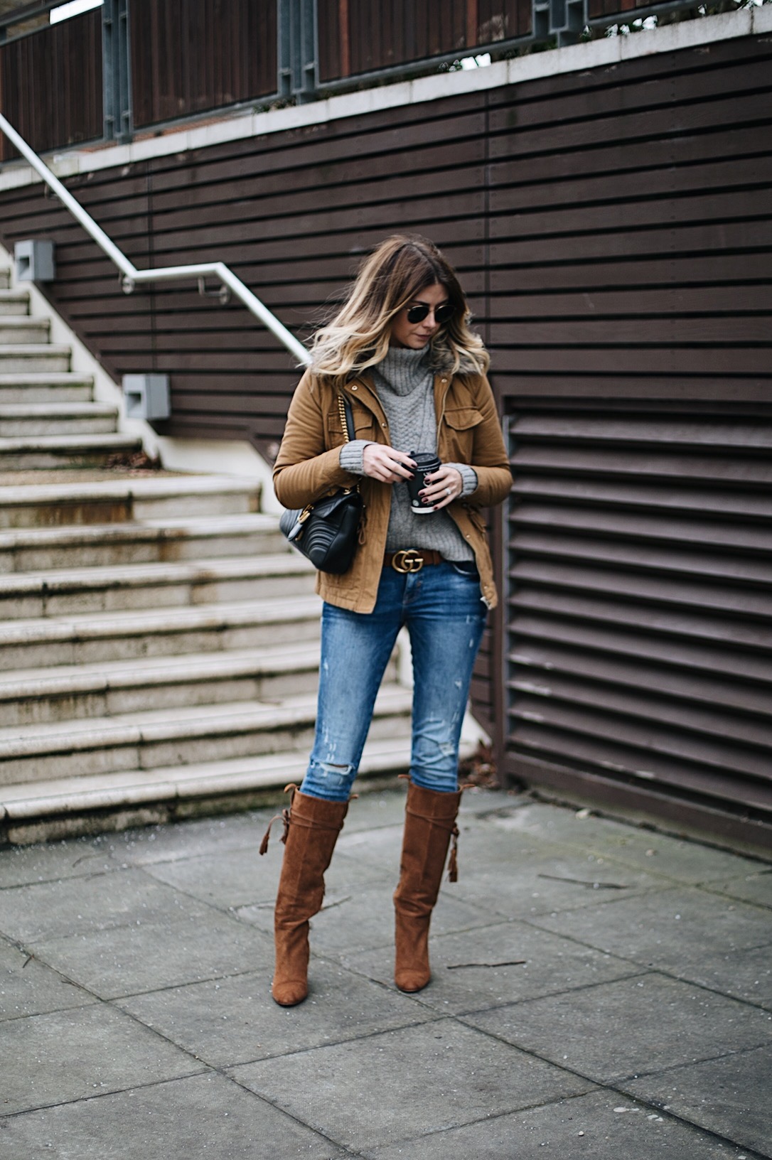 Emma Hill wears tan jacket, Grey cable knit sweater, tan Gucci marmont GG belt, ripped skinny jeans, tan suede knee high boots, black leather medium Gucci Marmont bag, chic winter outfit