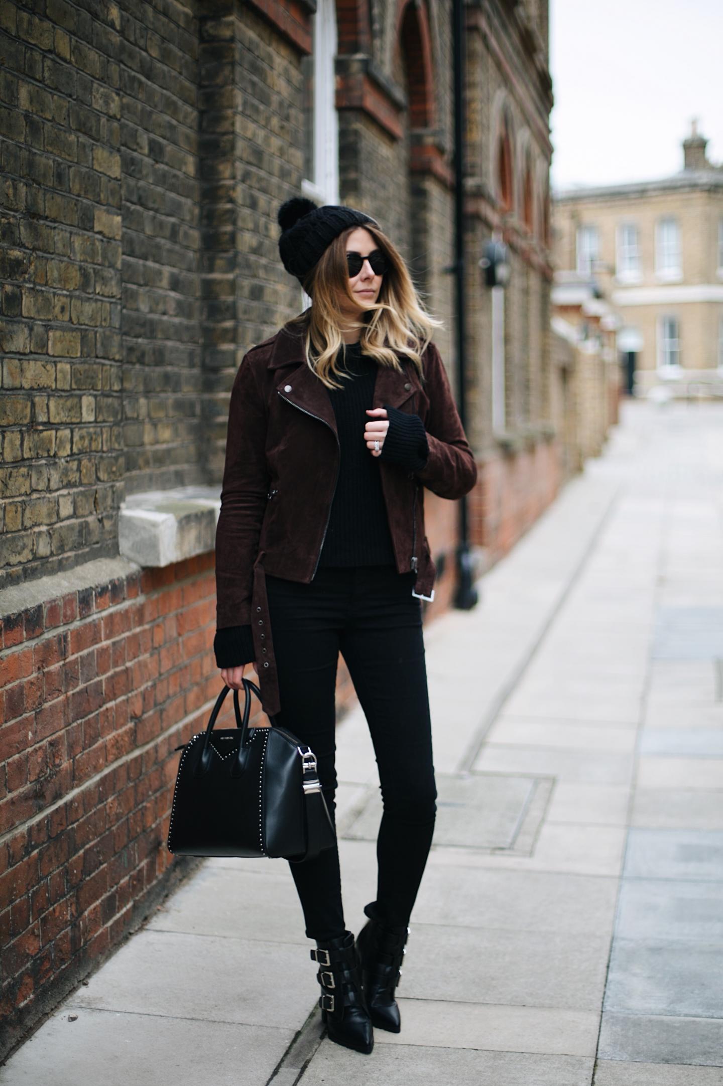 Emma Hill wears brown suede jacket, black skinny jeans, black sweater, knitted bobble hat, buckled heeled ankle boots, studded Givenchy Antigona bag, Round Rayban sunglasses, winter outfit ideas