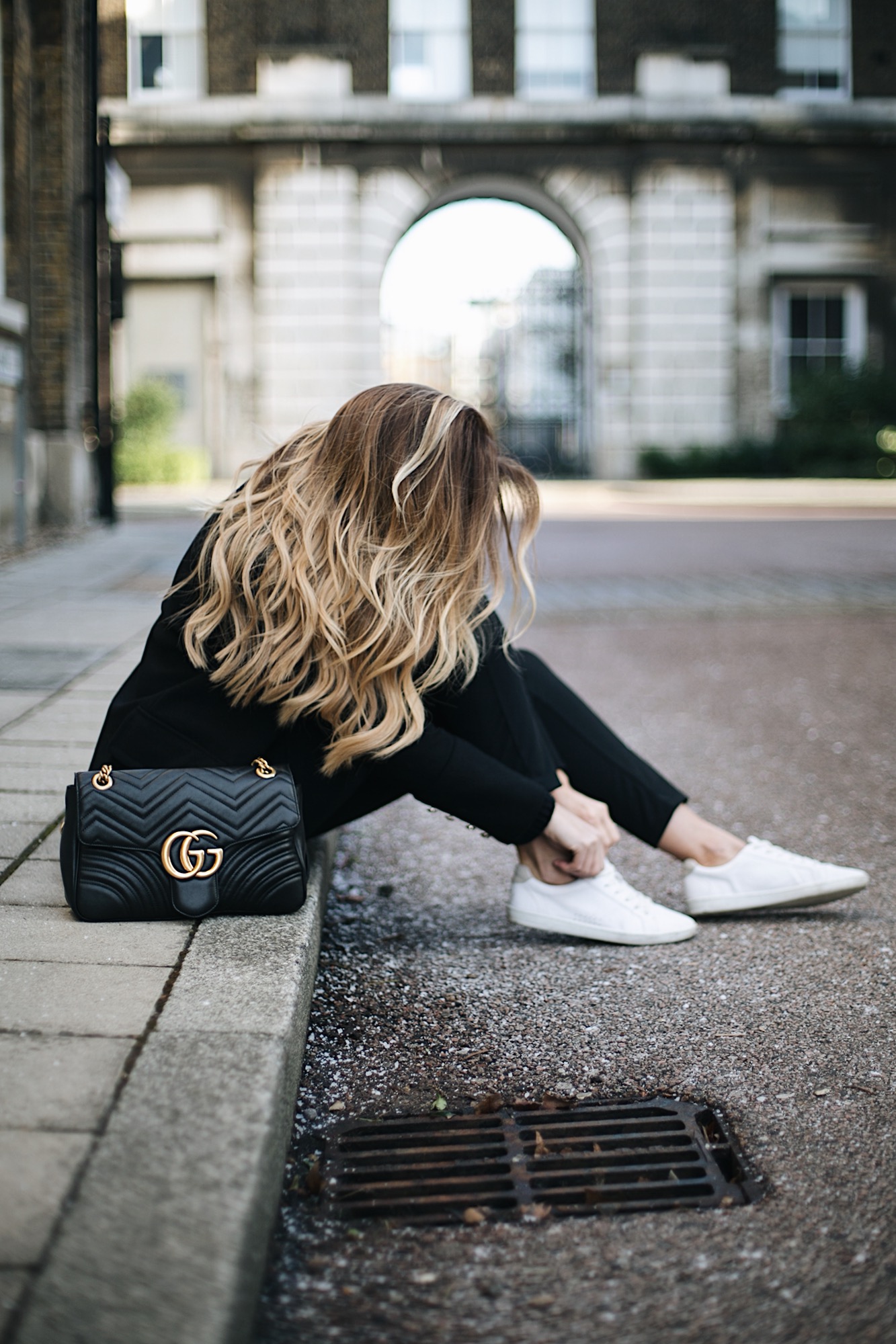 Emma Hill wears Gucci Marmont bag, black tailored trousers, black military jacket, white trainers, chic all black winter outfit