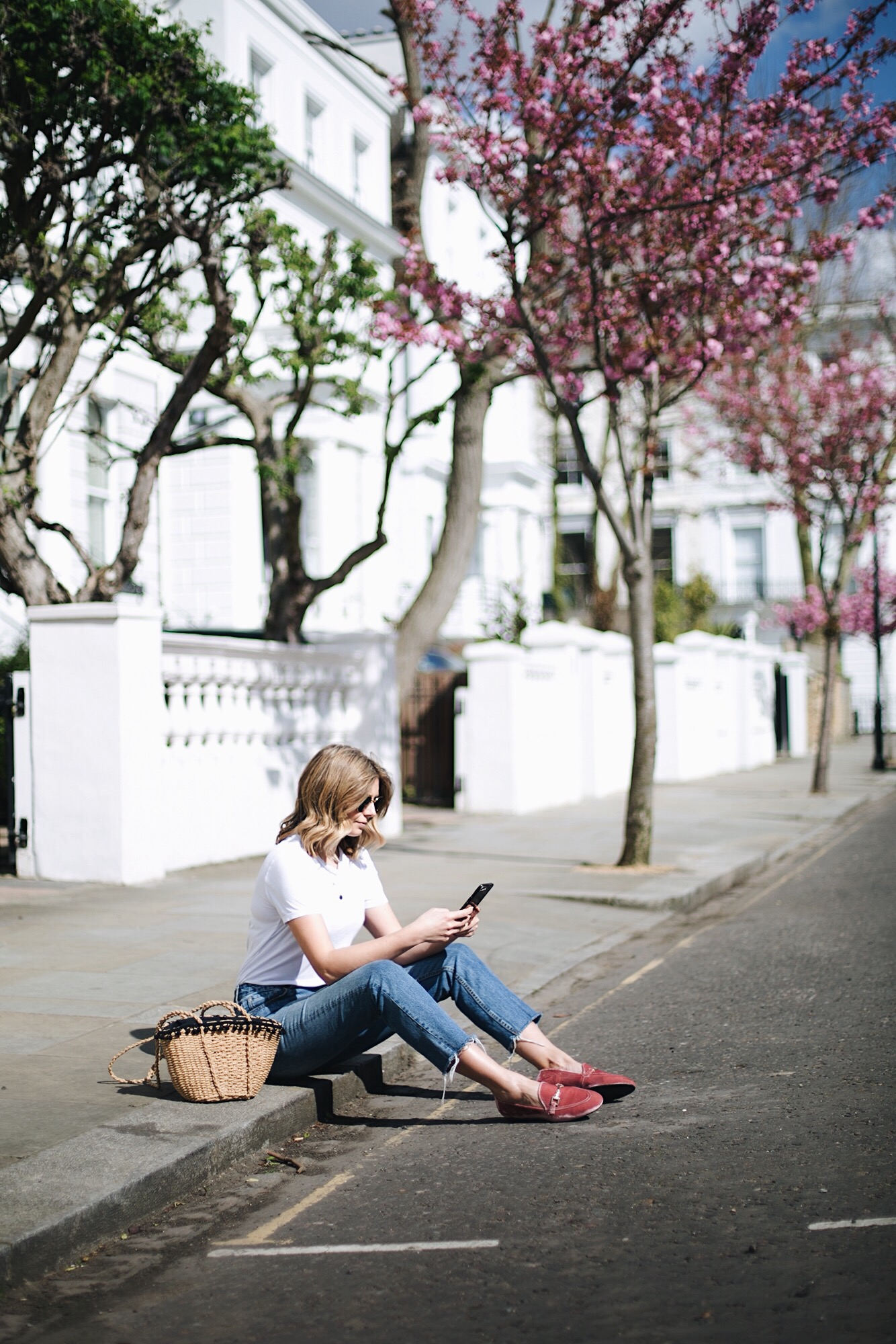 Emma Hill wears pink velvet loafers, raw hem jeans, basic white t-shirt, straw basket bag with pom poms