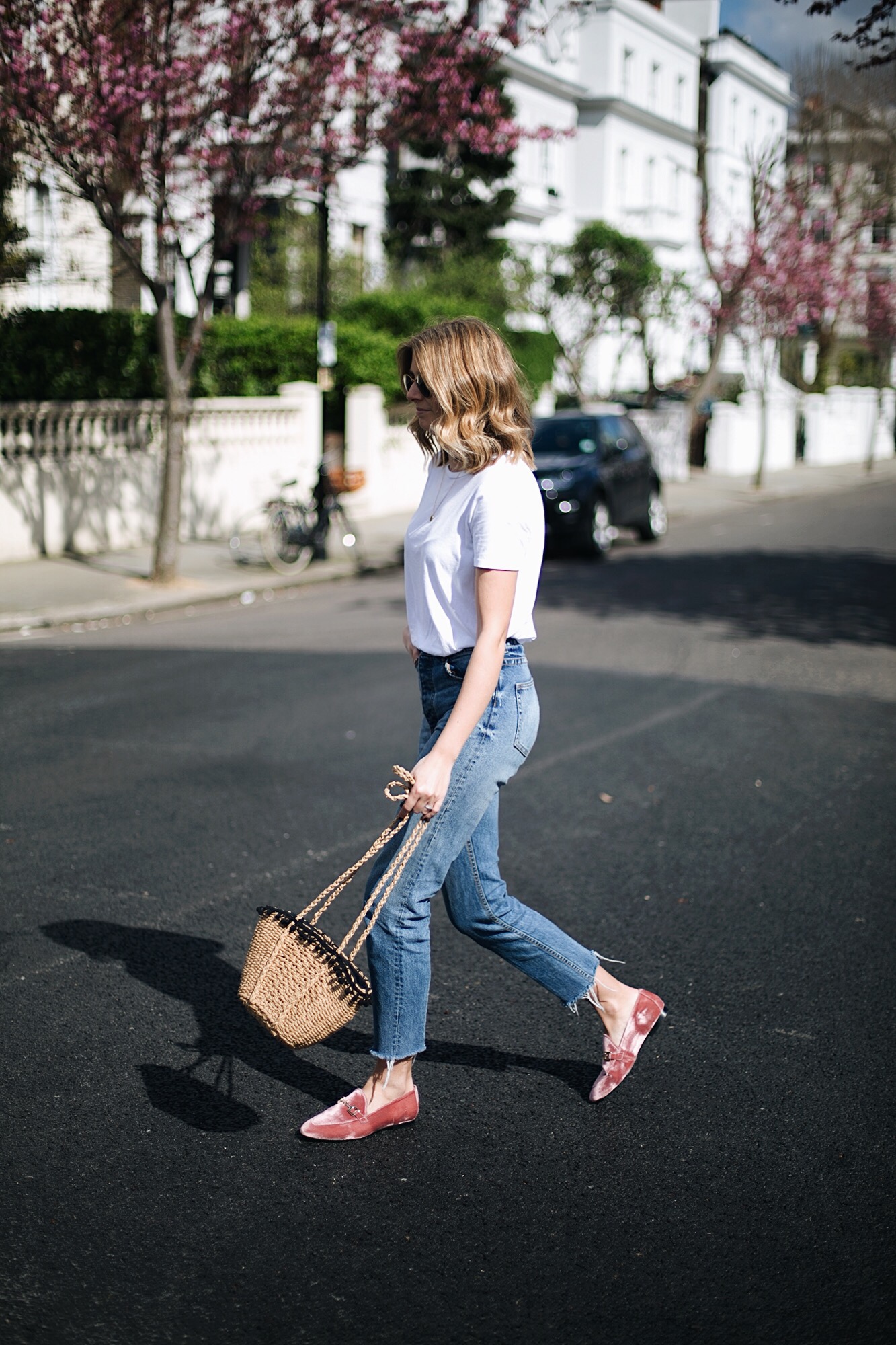 Emma Hill wears pink velvet loafers, raw hem jeans, basic white t-shirt, straw basket bag with pom poms