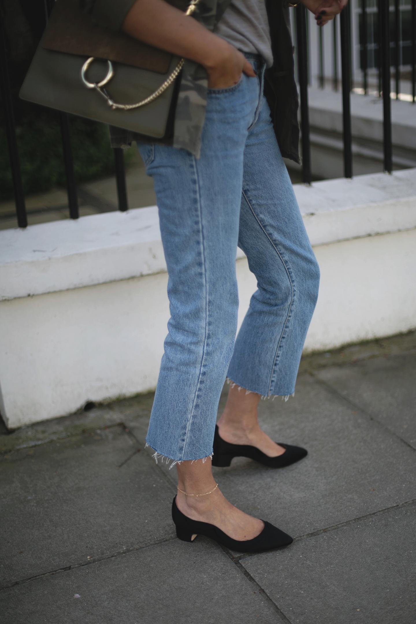 Emma Hill wears khaki Chloe Faye bag, cropped mid wash frayed hem jeans, dune x Super Sanderson black satin low block heels, camo jacket, grey t-shirt