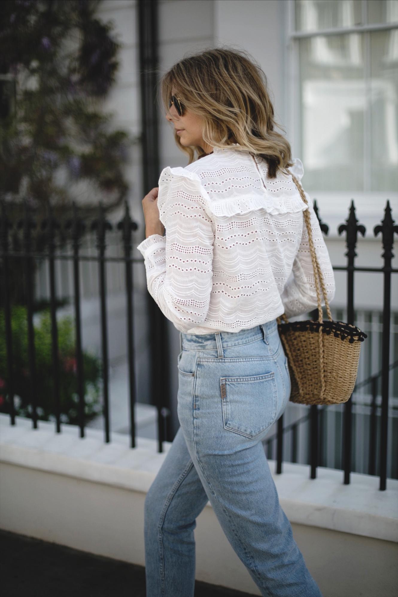 Emma Hill wears cream broderie anglais blouse, bleach wash high waisted jeans, straw basket bag with pom poms