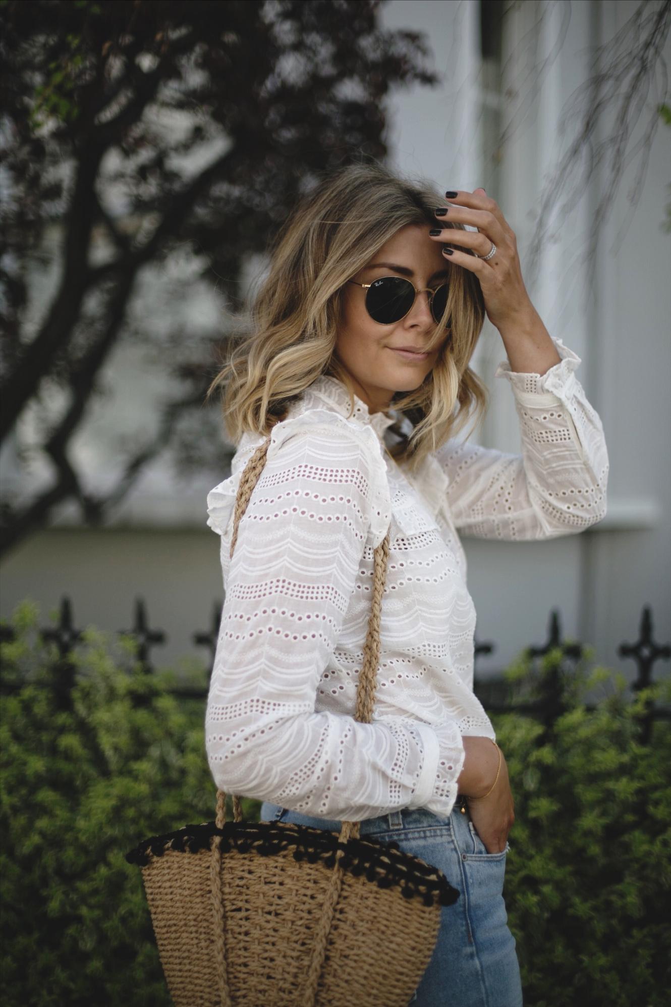 Emma Hill wears cream broderie anglais blouse, bleach wash high waisted jeans, straw basket bag with pom poms