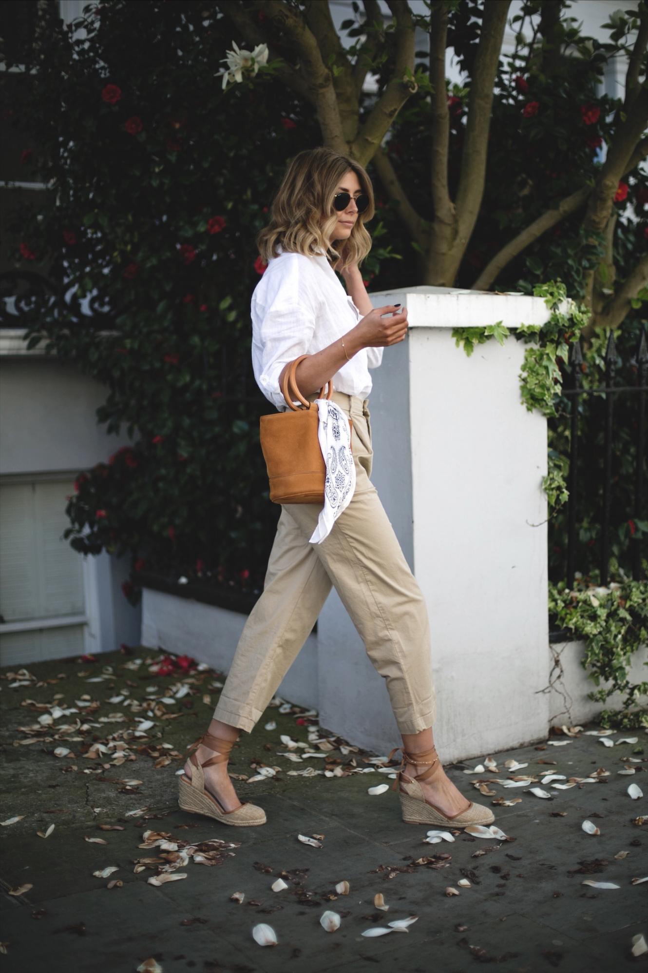 Emma Hill wears white linen shirt, beige chinos, natural wedge espadrilles, tan suede Simon miller bonsai bag with ring handle, chic spring outfit