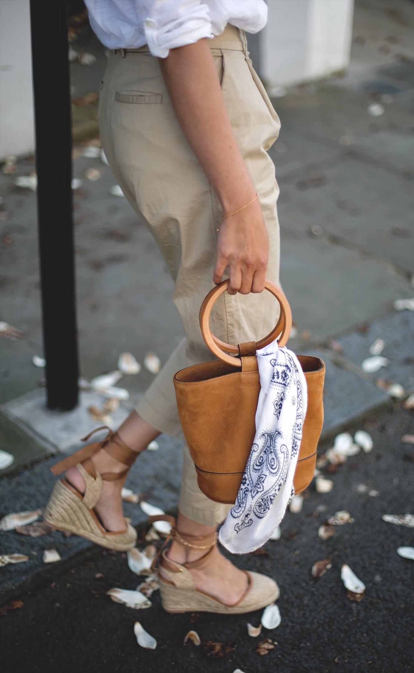 Emma Hill wears white linen shirt, beige chinos, natural wedge espadrilles, tan suede Simon miller bonsai bag with ring handle, chic spring outfit