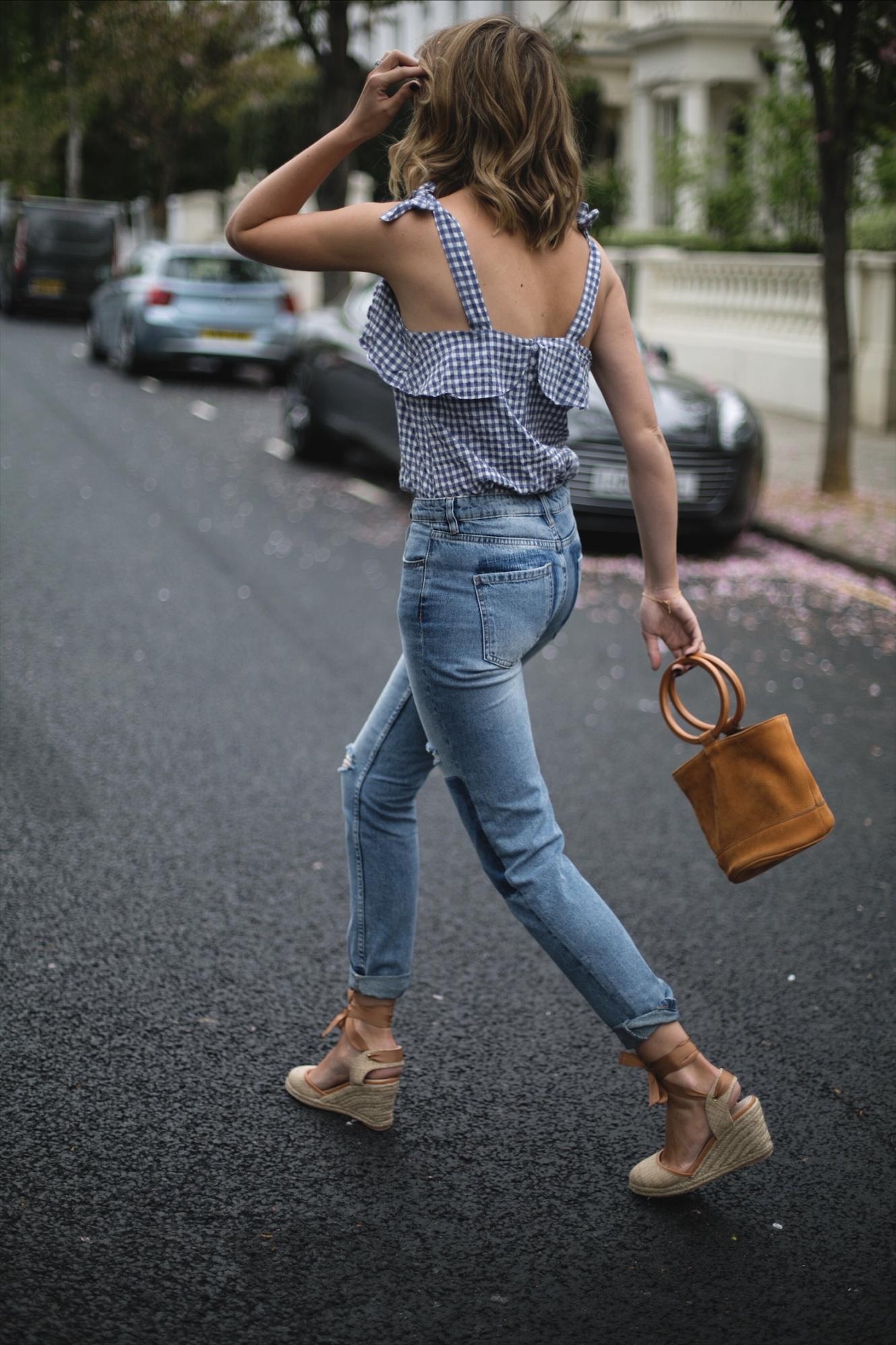 Emma Hill wears gingham top, rolled up hem jeans, wedge espadrilles, tan suede Simon Miller ring handle bag