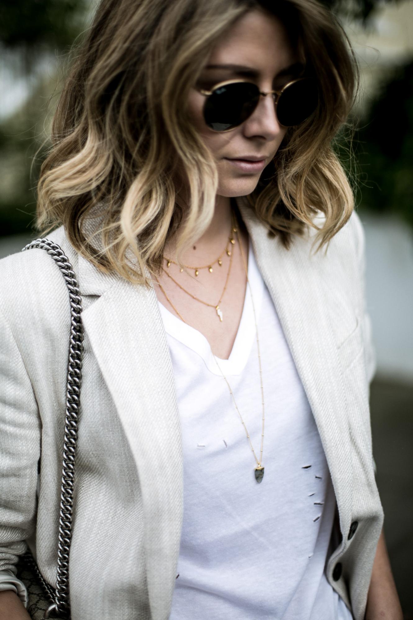 Emma Hill from EJSTYLE wears gold layered necklaces, white nibbled t-shirt, beige linen blazer, gold round Ray-Ban sunglasses
