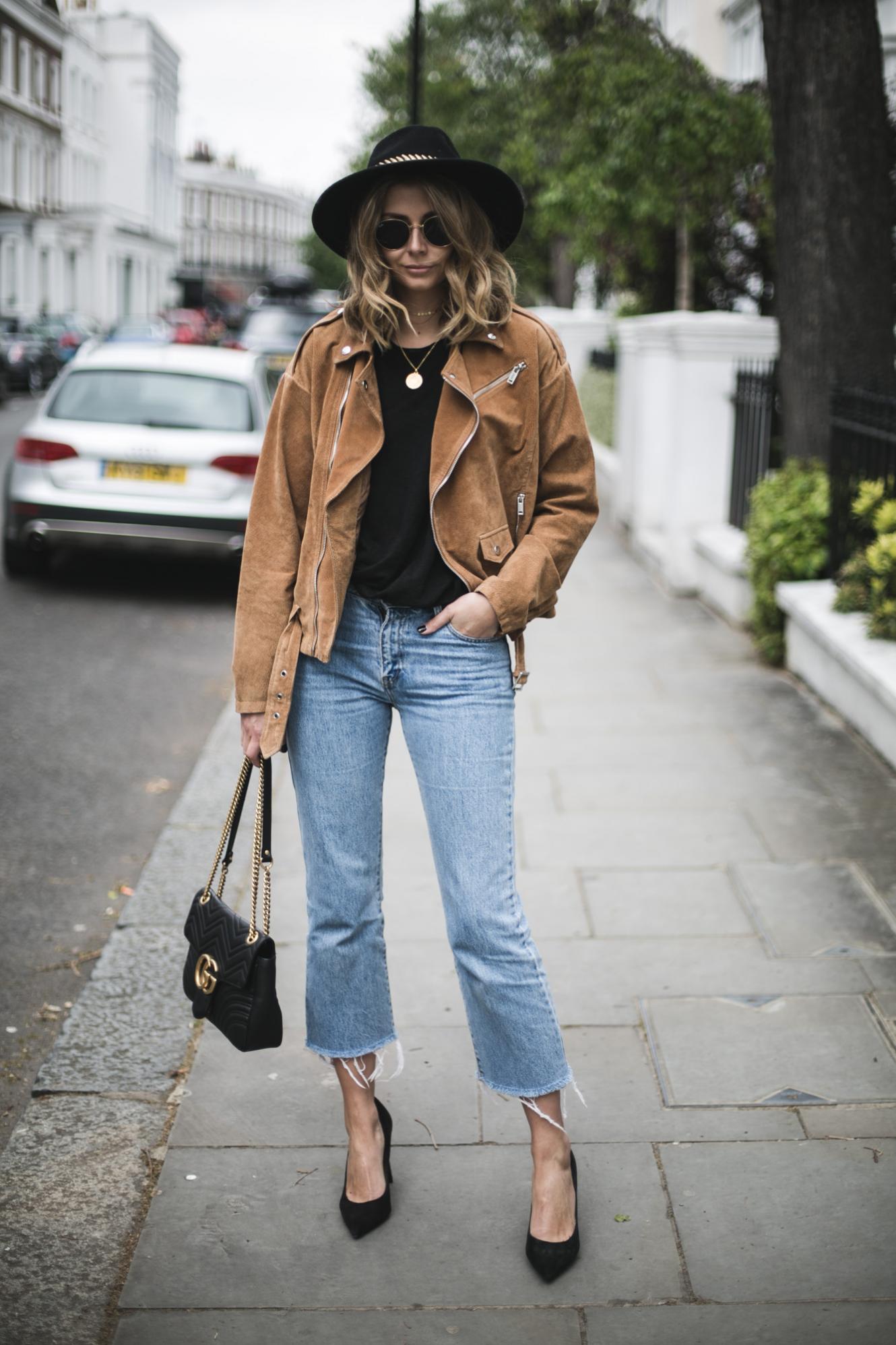 Emma Hill from EJSTYLE wears tan suede biker jacket, black t-shirt, cropped flare raw hem jeans black Gucci Marmont bag, Black suede heeled pumps, black fedora, spring outfit