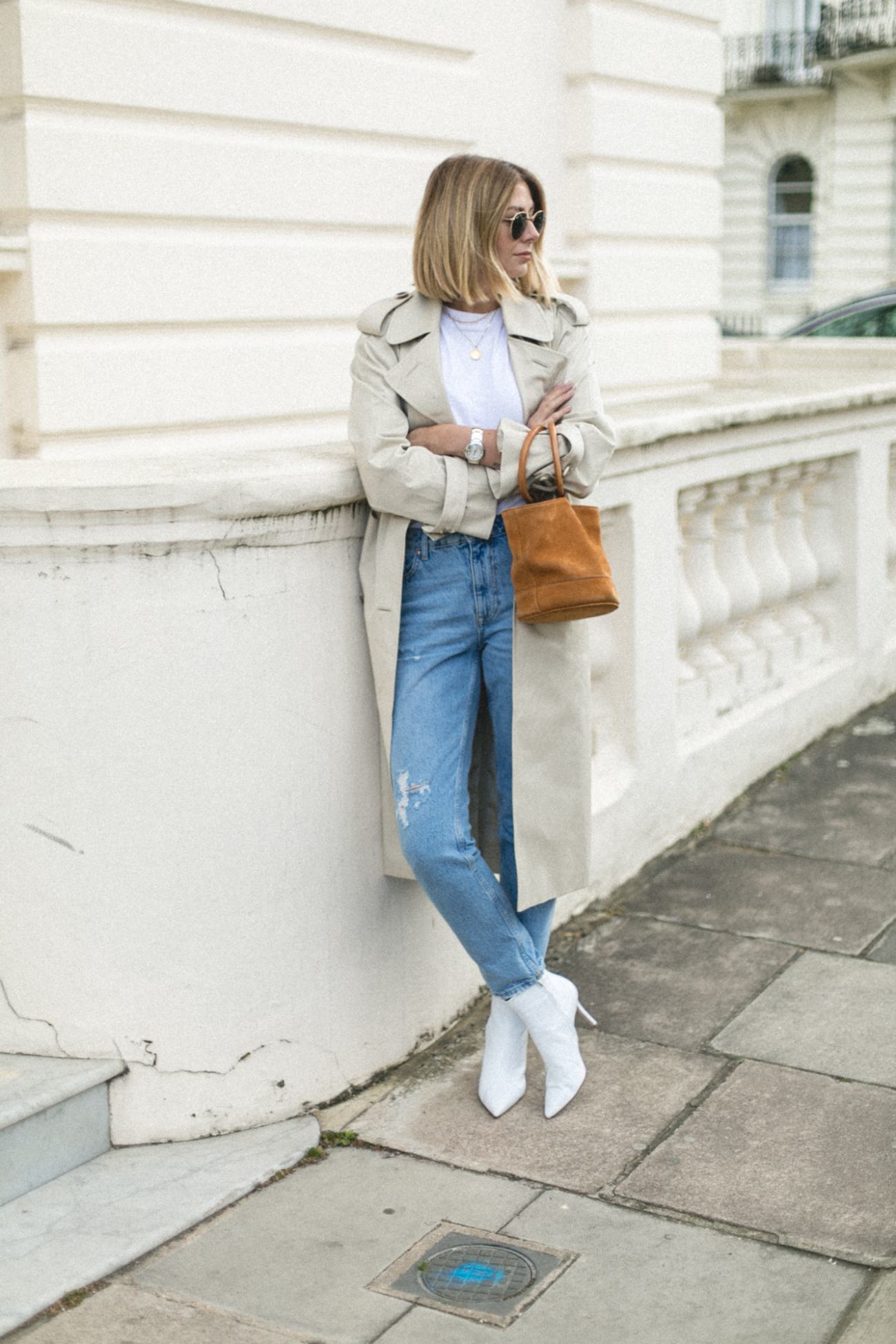 Emma Hill wearing Trench coat, light wash jeans, white ankle boots, Simon Miller tan nubuck Bonsai bucket bag, chic Spring outfit