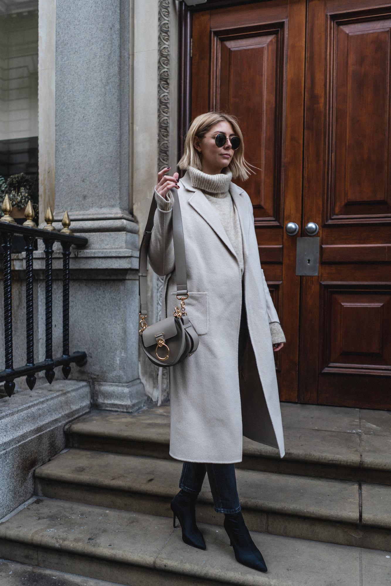 Emma Hill style. Chic winter outfit. Cream wool belted coat, Chloe Tess bag, cropped black wash jeans, black sock boots, beige chunky knit jumper-2