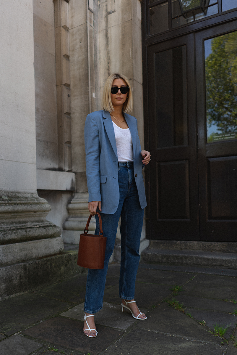 Emma Hill style, black Ray Bay sunglasses, blue linen blazer, white linen vest top, brown tan leather bucket bag, straight leg jeans, white strappy sandals, chic spring summer outfit