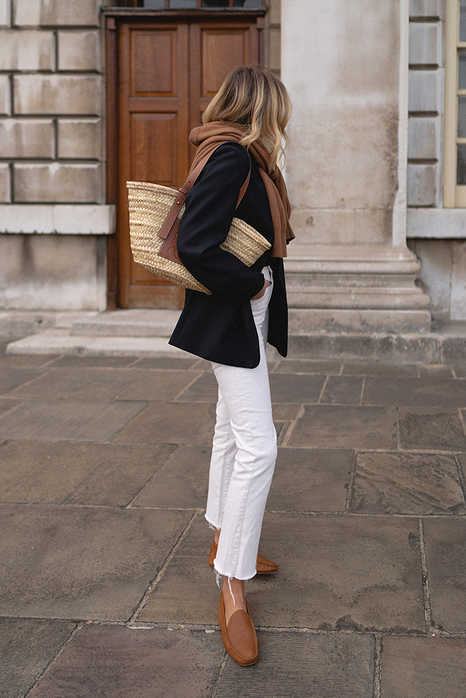 Emma Hill style, classic black blazer, tan cashmere jumper worn over shoulders, white jeans, Loewe basket bag, tan leather loafers. Autumn outfit_