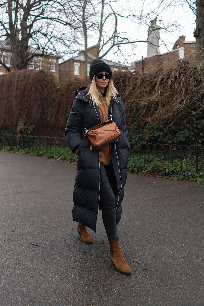 Emma Hill style. Black long puffa coat, black beanie hat, tan jumper, black skinny jeans, tan suede Saint Laurent ankle boots, Tan leather Loewe Puzzle bag. Casual Winter outfit