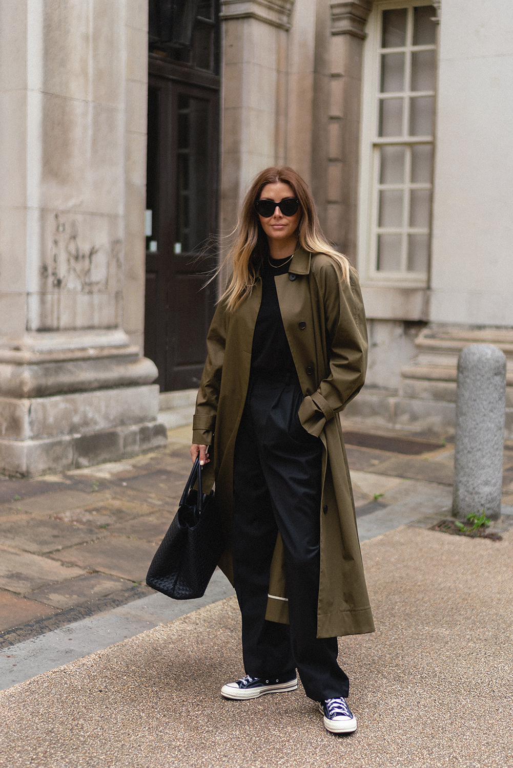 Emma Hill wears green trench coat, black t-shirt, black tailored trousers, celine Baby Audrey sunglasses, black Bottaga Veneta intrecciato tote bag, Converse chuck 70 high tops, chic Autumn Fall outfit