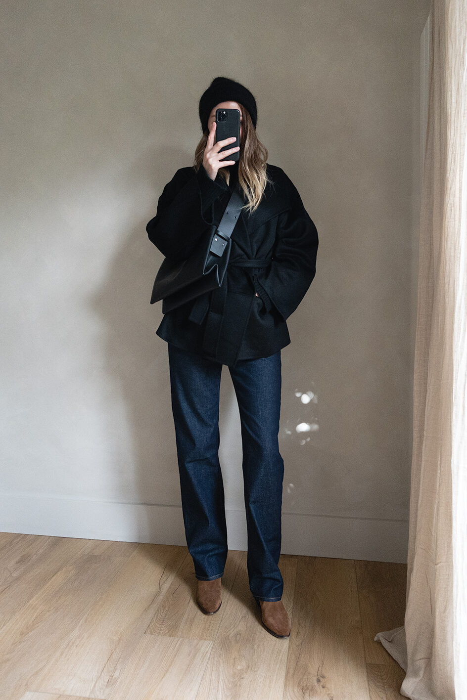 Emma Hill style. Black beanie hat, black wrap jacket, black cross body bag, dark wash straight leg jeans, tan suede ankle boots. Chic Autumn Winter outfit
