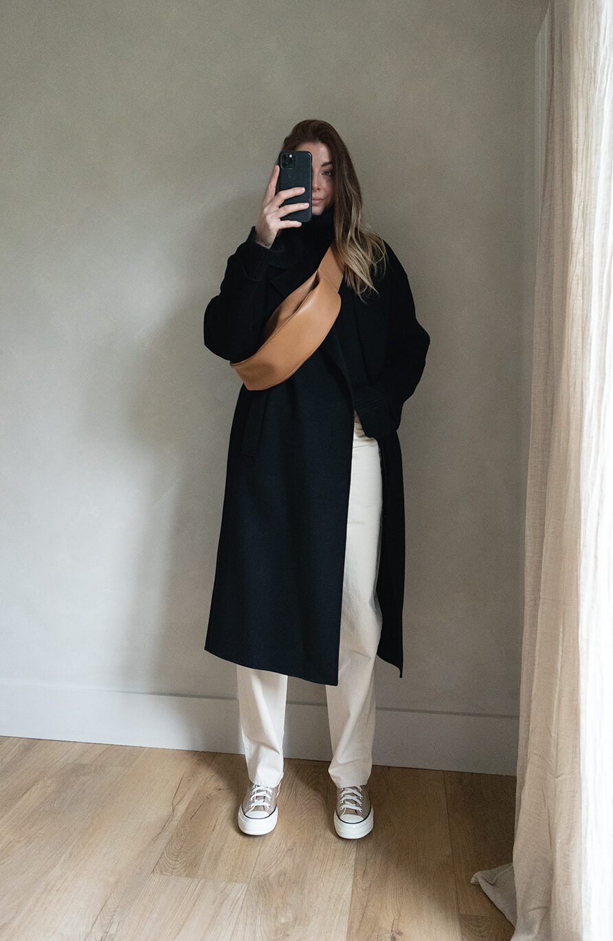 Emma Hill style. Black long coat, cream off white straight jeans, khaki Converse Chuck 70 high top trainers, black jumper, tan leather slouchy cross body bag. Chic casual Winter outfit