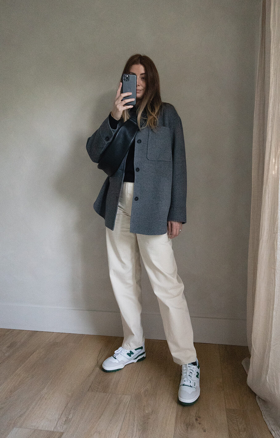 Emma Hill style. Grey wool shacket overshirt, black jumper, cream off white tapered jeans, New Balance 550 white and green, Black cross body sling bag. Casual Spring outfit