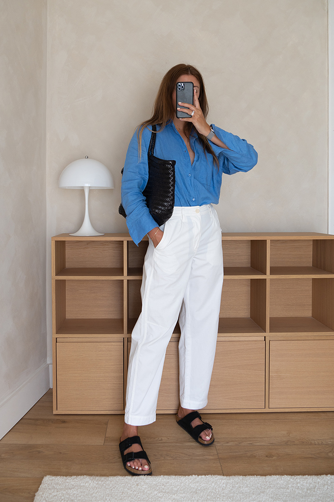 Emma Hill Summer style. Mid blue linen shirt, white cropped trousers, black Birkenstock arizona sandals, black Dragon Diffusion Nantucket bag. Minimal Summer outfit