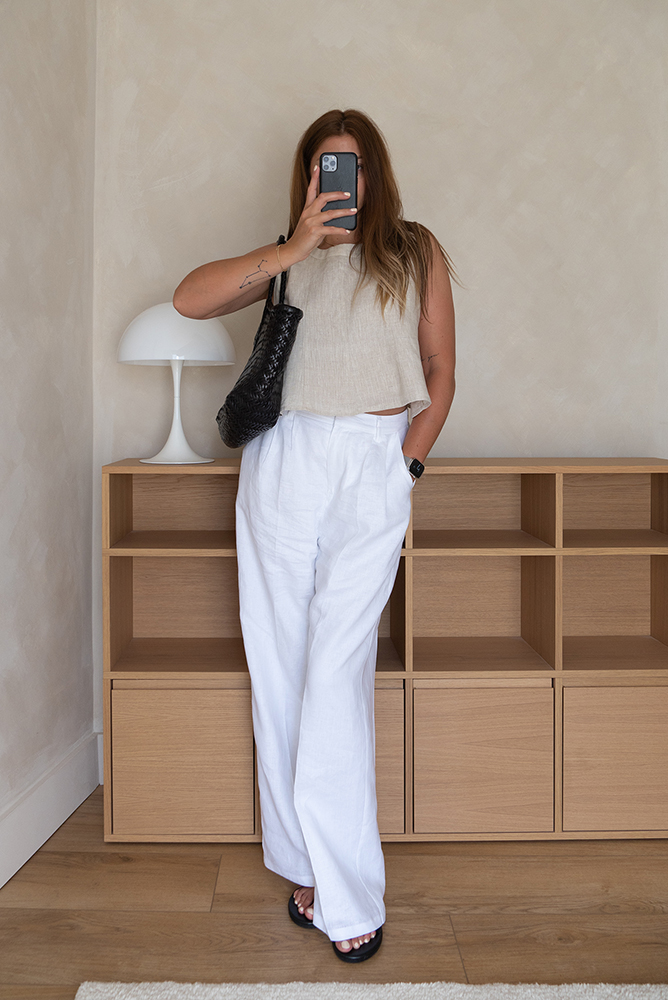 Emma Hill style. Beige linen cropped sleeveless top, white linen tailored trousers, black sandals, black Nantucket draggon diffusion bag. Chic, minimal Summer outfit