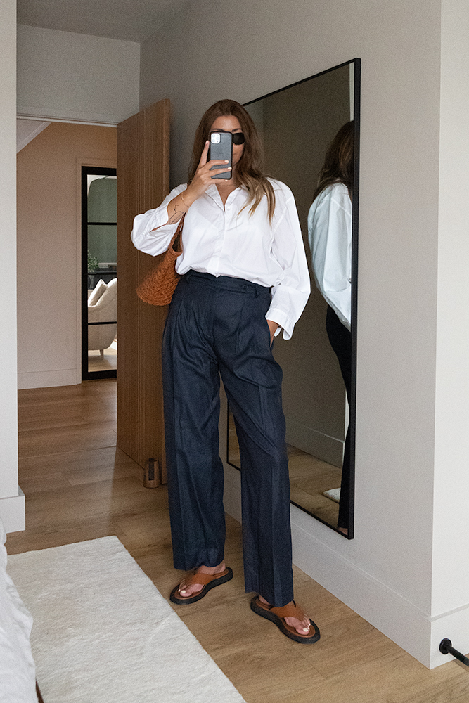 Emma Hill style. Crisp white button down cotton shirt, navy tailored trousers, tan woven leather Dragon Diffusion Triple Jump bag, tan leather thong sandals. Chic minimal Summer outfit