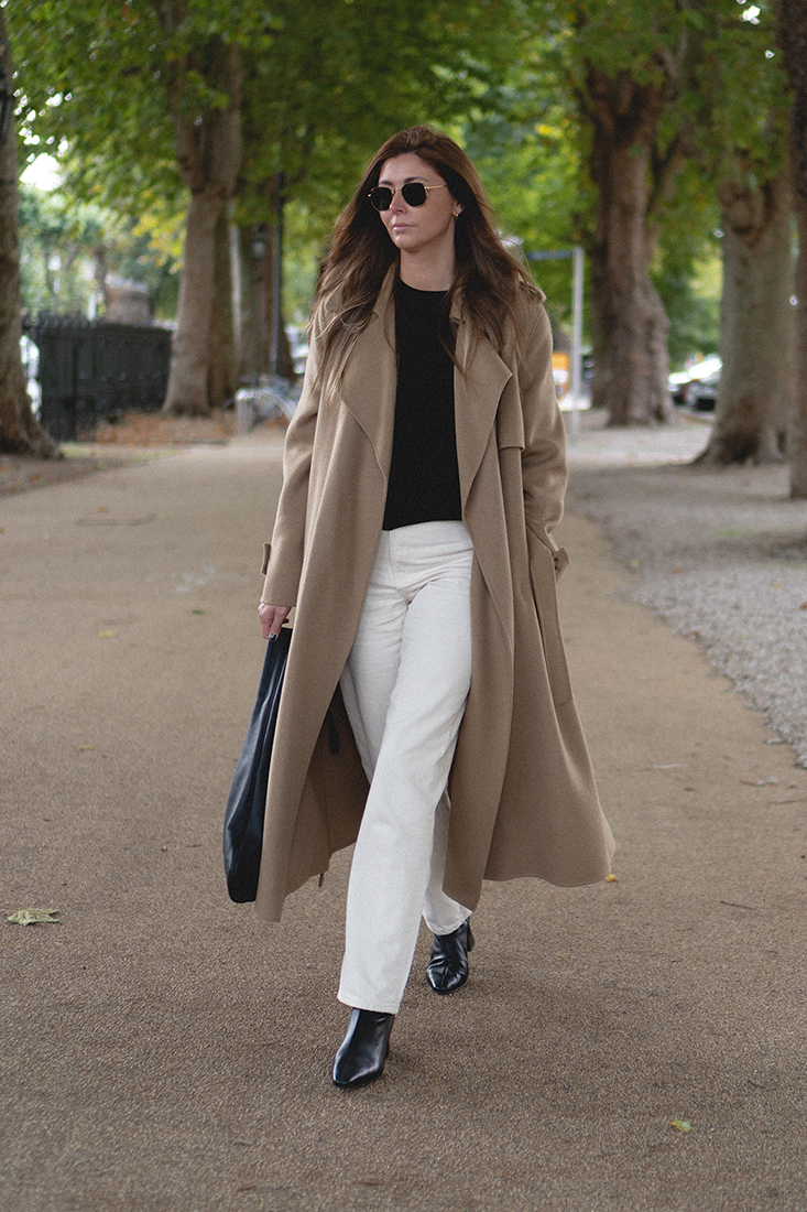 BLOG Emma Hill style. Camel wool long coat, black jumper, cream off white tapered jeans, black mid heel ankle sock boots, The Row medium Everyday shoulder bag. Chic Autumn outfit ideas