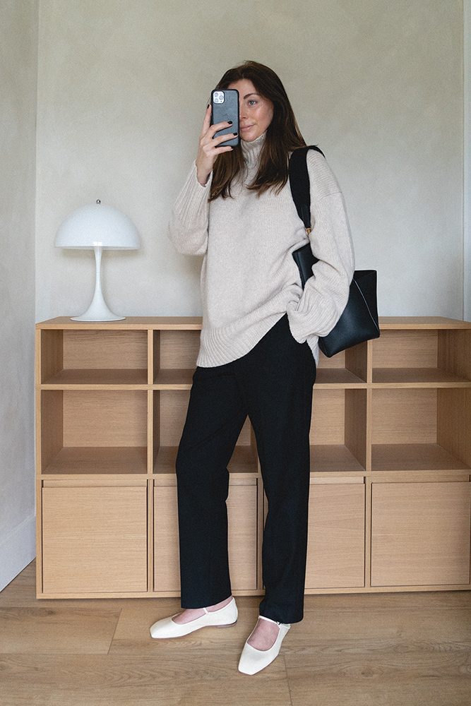 Emma Hill style. Transitional Spring Autumn outfit. Beige cashmere chunky jumper, black tailored trousers, off white Aeyde mary jane flats, Black Celine Bag. Minimal style